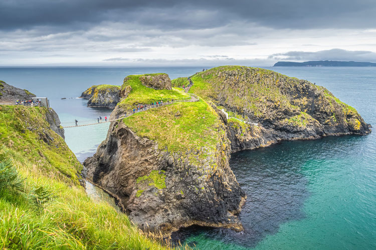 People on the carrick a rede rope bridge and scenic island surrounded by turquoise atlantic ocean