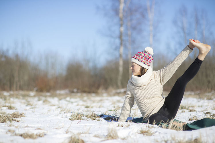 Young attractive woman practicing yoga on snowy field. outdoor sport activity. practice yoga asana. 