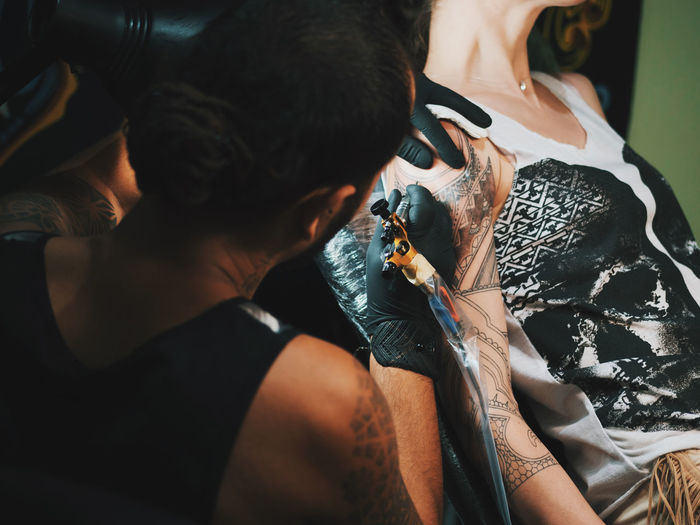 Tattoo artist making tattoo on hand of female customer
