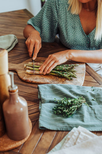 Midsection of a woman cutting asparagus on a cutting board at table