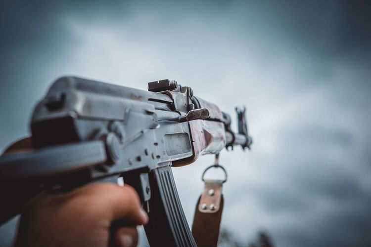 Close-up of hand holding weapon against sky