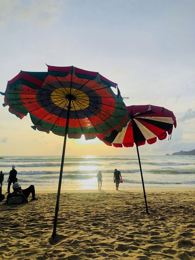 People and parasols at beach against sky during sunset