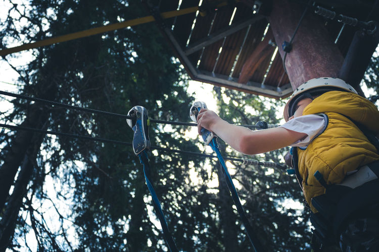 Low angle view of small boy attaching carabiner on a rope during canopy tour in adventure park.