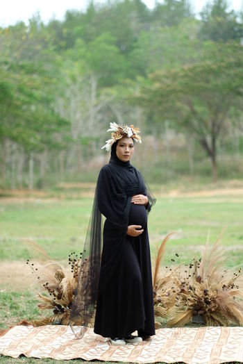 Full length of woman standing on field with black dress for maternity photo shoot