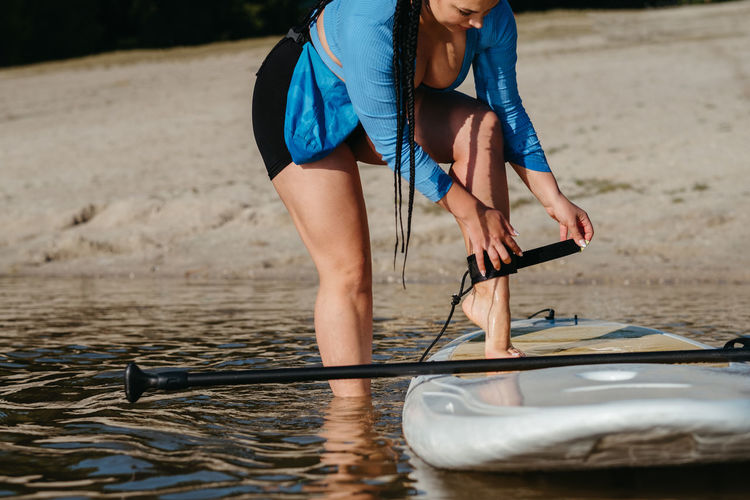 Woman attaching insurance cable of sup to her leg, preparing to swim on a board