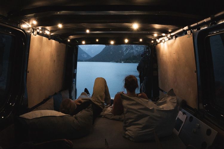 Rear view of people sitting in camper view on lake