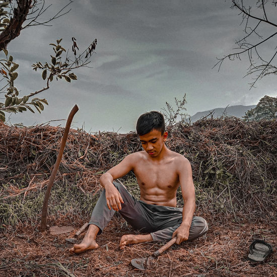 Young man sitting on land against sky