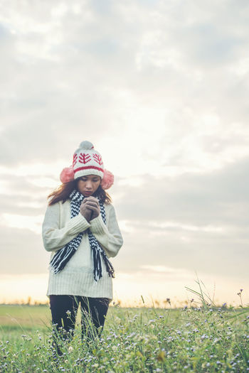 Woman in warm clothing standing on field against cloudy sky