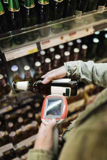 Cropped image of female customer scanning beer bottle in supermarket