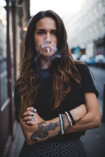 Portrait of young woman smoking while standing on footpath
