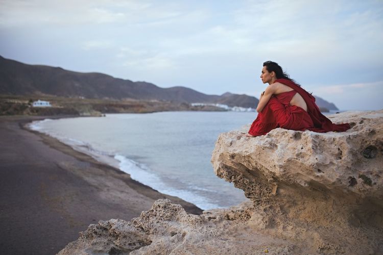 Woman in red dress sitting on rock formation