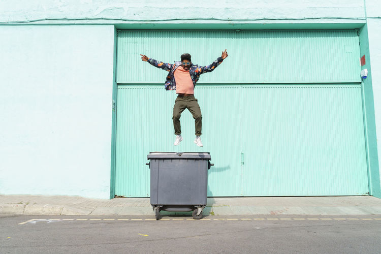 Carefree man jumping from garbage bin on sunny day
