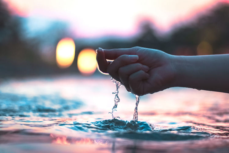 Hand holding water against sky during sunset