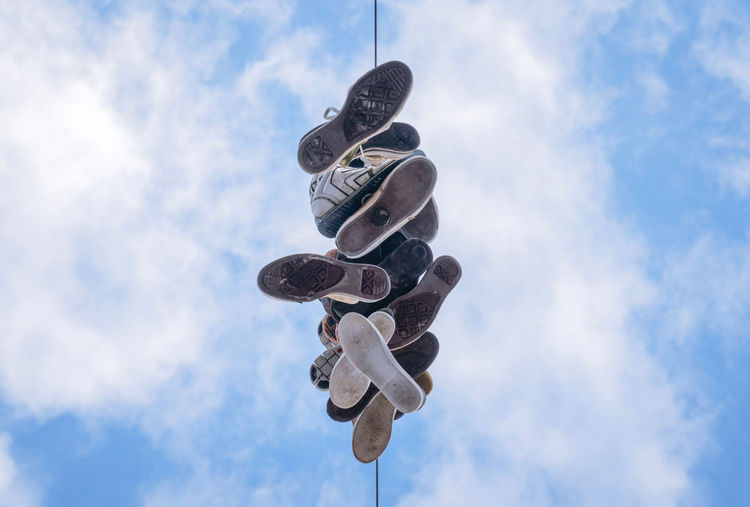 Low angle view of shoes hanging on string against cloudy sky