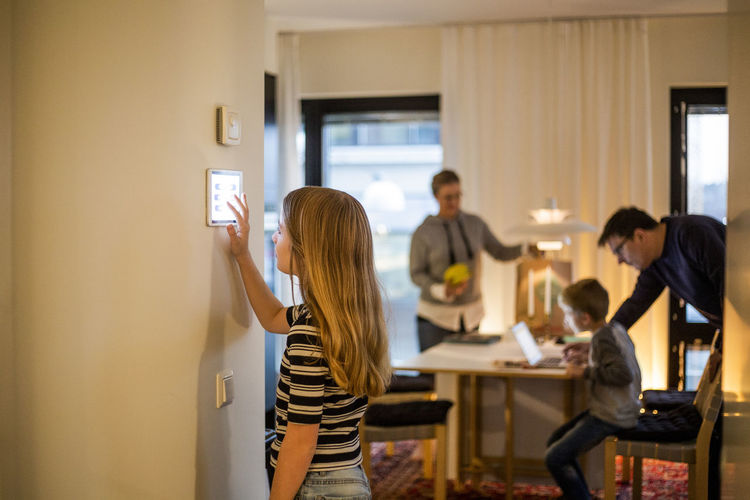 Girl using digital tablet on wall with family in background at smart home