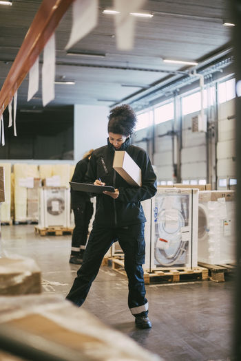 Businesswoman writing on clipboard while analyzing packages at warehouse