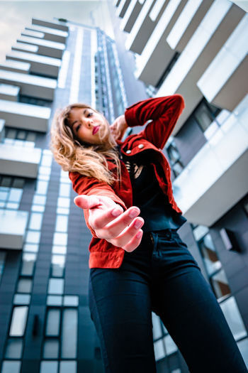 Low angle portrait of young woman standing against buildings in city