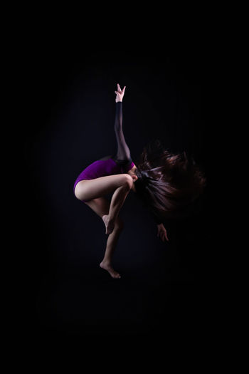 Side view of woman dancing against black background