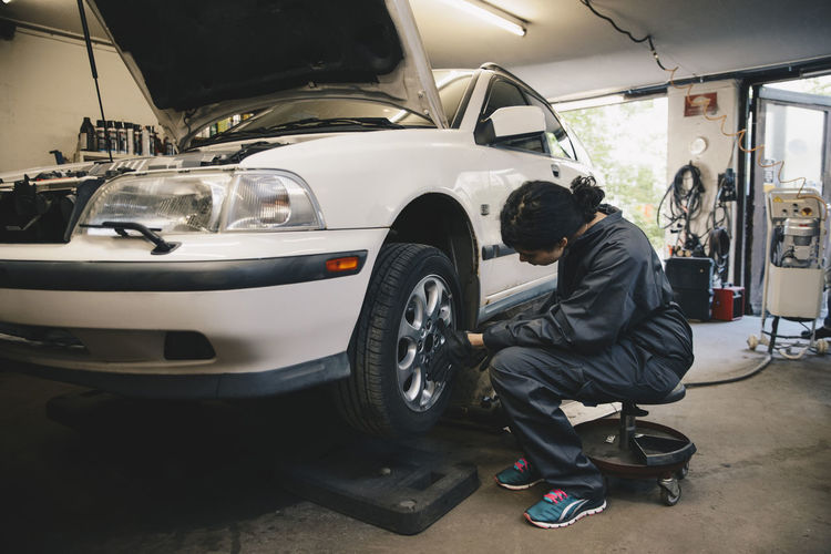 Side view of female mechanic examining car wheel at auto repair shop