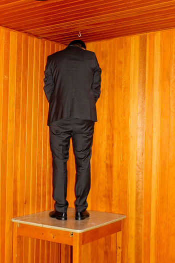 Rear view of man in formalwear standing on table against wall