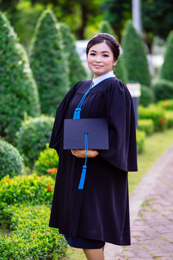 Portrait of smiling young woman wearing graduation gown standing outdoors