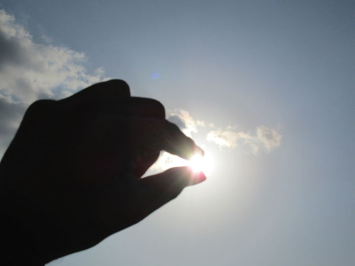 Silhouette hand holding sun against sky