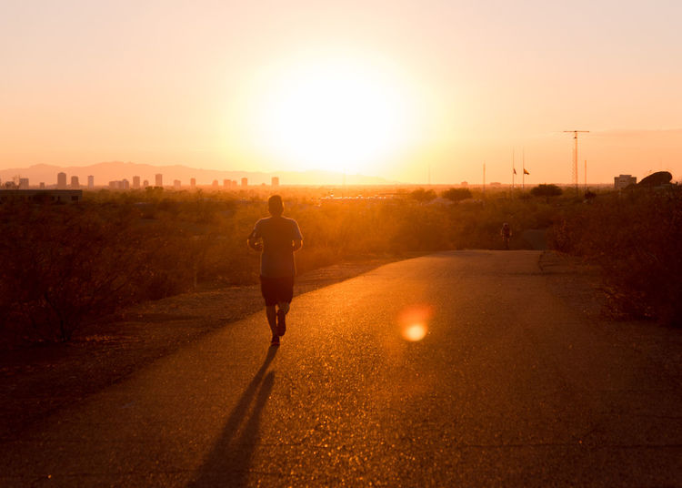 Rear view of man jogging on road during sunrise