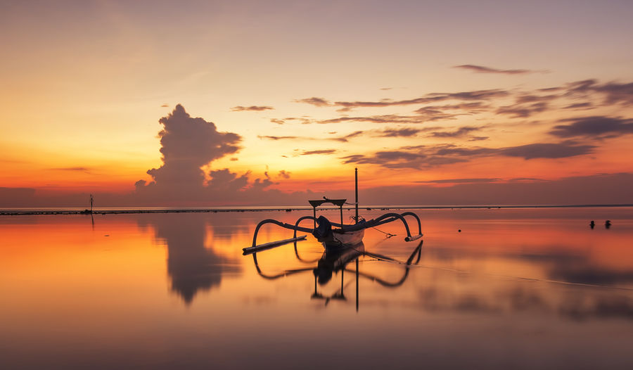 Jukung moored on shore against sky during sunrise