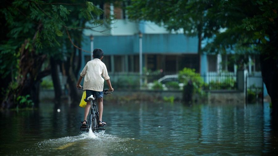 Rear view of boy with his bike in water on a rainy day 