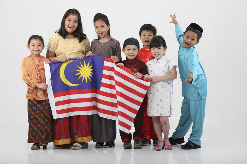 Full length portrait of children holding malaysian flag on white background