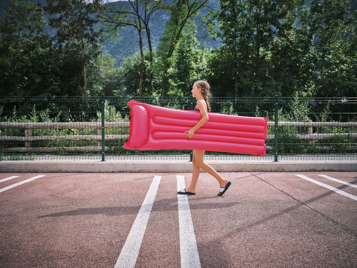 Smiling girl walking with inflatable pink pool raft in parking lot