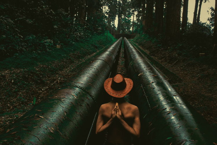 Woman doing yoga amidst water pipes in forest