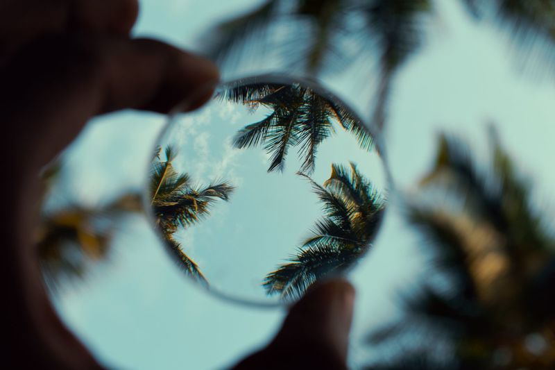 Close-up of hand holding lens against sky