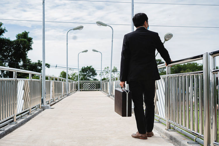 Asian businessman holding briefcase walking on overpass looking outside