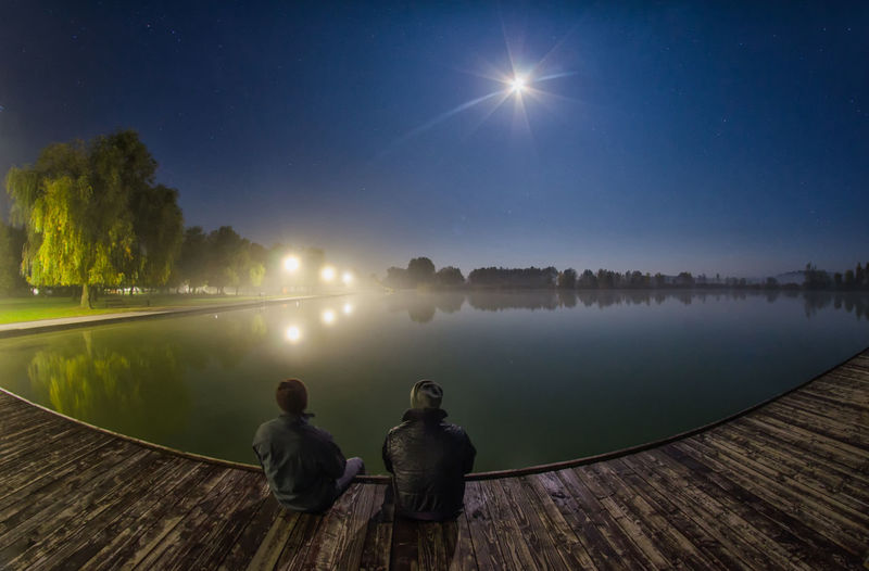 Rear view of people on lake against sky at night