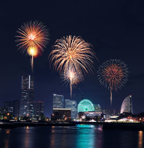 Firework display over river and illuminated cityscape at night