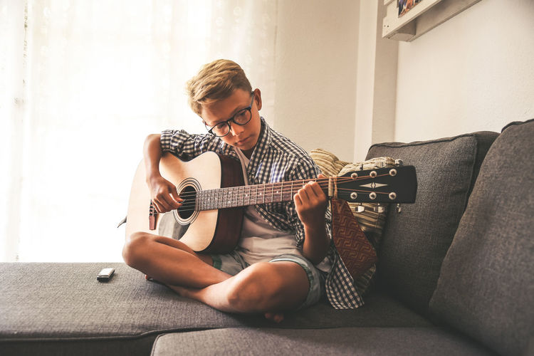 Full length of boy playing guitar while sitting on sofa at home