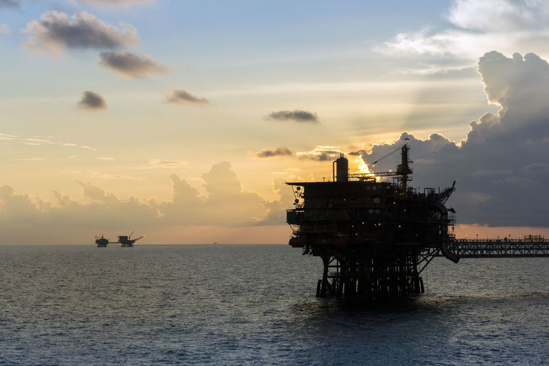 Seascape of oil field with silhouette of oil production platform during sunset at offshore oil field
