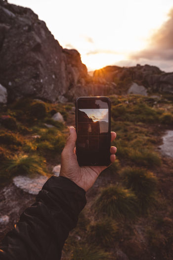 Hand holding smartphone with image of scene backlit by sunset