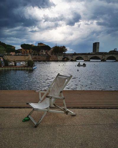 Chair by river against buildings in city