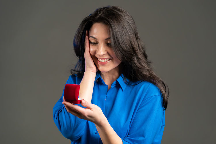 Smiling woman holding smart phone while standing against blue background