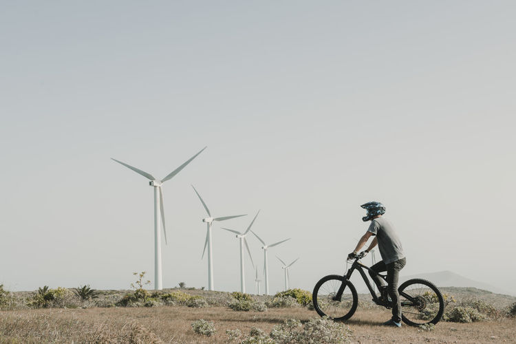 Spain, lanzarote, mountainbiker on a trip in desertic landscape with wind turbines in background