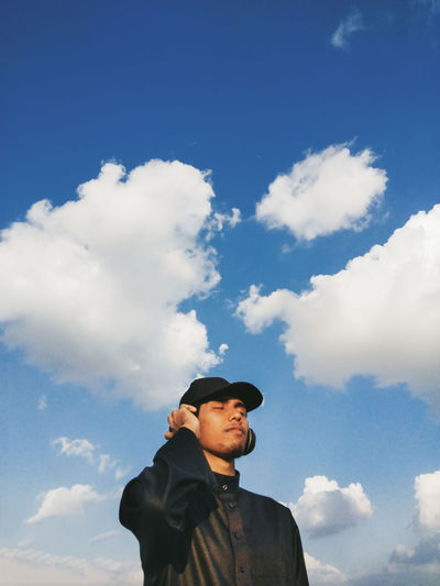 Low angle view of man listening music against sky