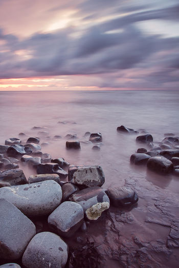 Stones at sea shore against sky during sunset