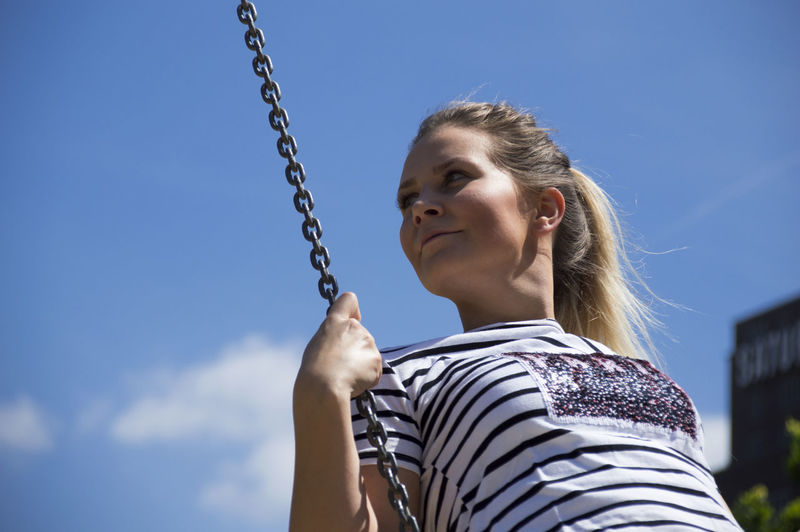 Low angle view of young woman looking away while swinging against sky