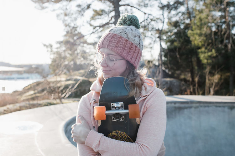 Woman sat with her eyes closed holding her skateboard in a skatepark