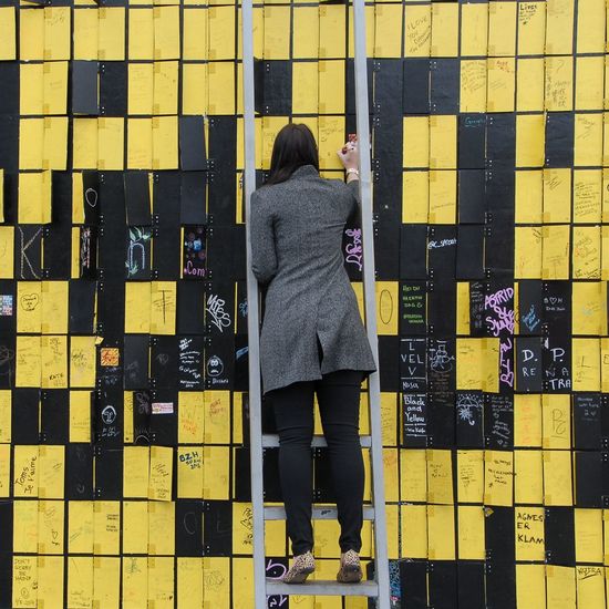 Rear view of woman standing against yellow wall