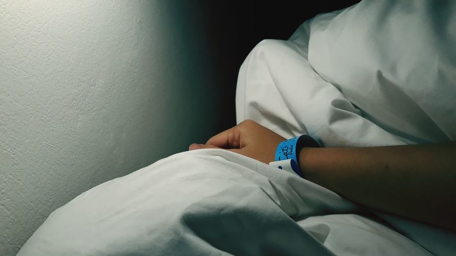 Close-up of patient wearing hospital identification bracelet on bed sheet in hospital