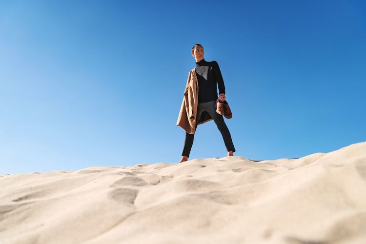 Low angle view of man standing on desert against clear blue sky