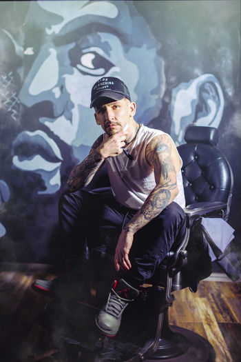 Portrait of man sitting on chair against graffiti wall